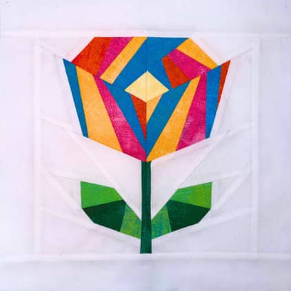Linda's exclusive free Shop Hop quilt block — a colorful geometric flower block with a yellow diamond center and orange, pink, and blue striped petals