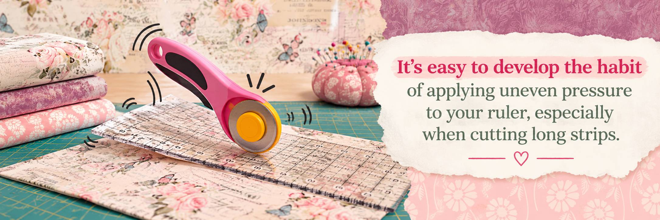 A wide, brightly lit craft workspace shows a pink-and-orange rotary fabric cutter resting on a transparent gridded ruler laid diagonally across floral...