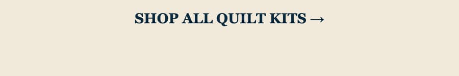 A wide, minimal banner with a warm cream background and centered dark navy serif text reading “SHOP ALL QUILT KITS →”; the text is large and bold, wit...