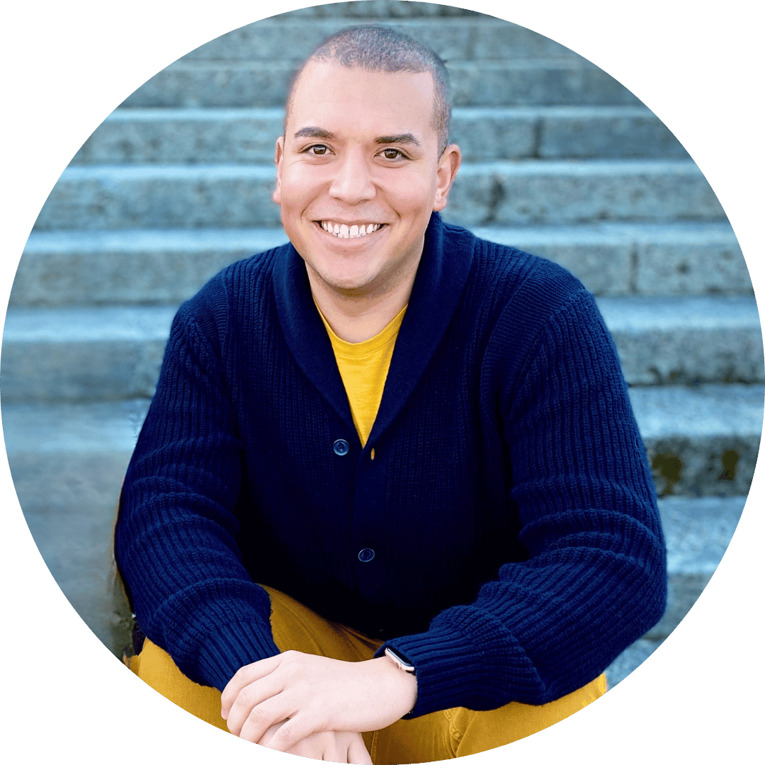 A medium shot shows a man with short hair wearing a yellow t-shirt and a dark blue cardigan with two buttons, sitting on gray concrete stairs, with hi...