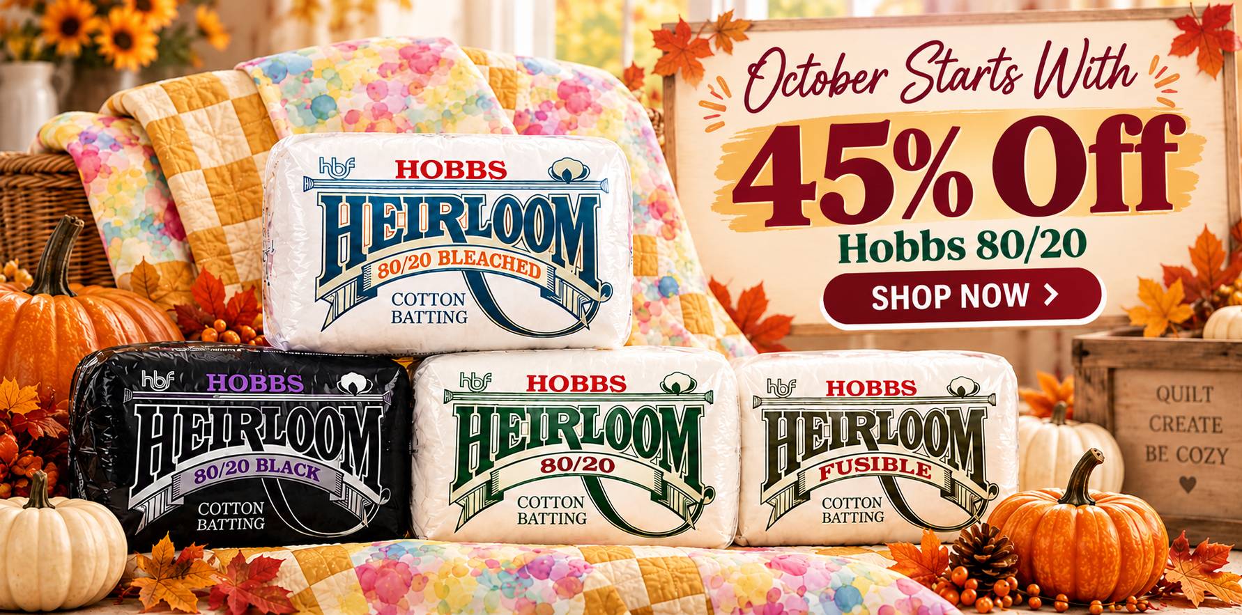 A wide, brightly lit autumn display shows four stacked Hobbs Heirloom cotton batting packages in white, black, and cream, in front of a multicolored p...